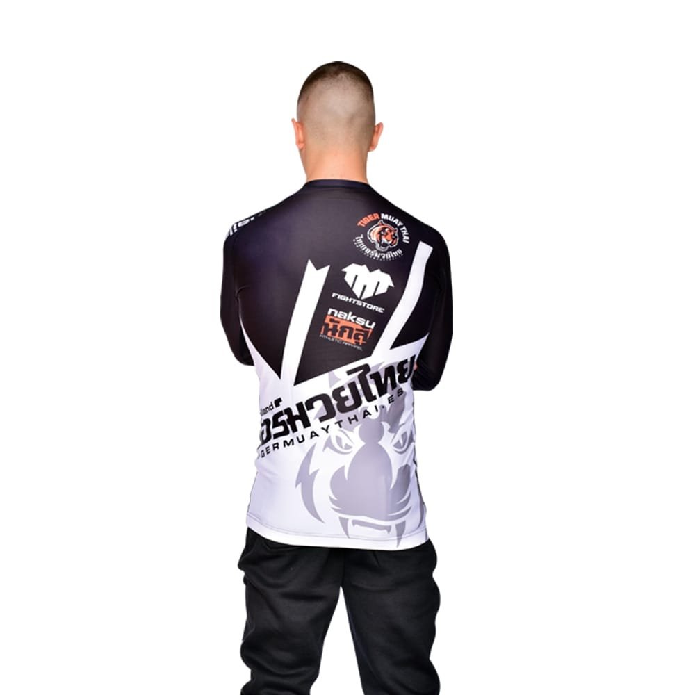 Camiseta deportiva Rash Guard de la marca "Tiger Muay Thai" de color blanco, gris y negro. Llevada por modelo con brazos estirados. Transpirable con diseño sublimado. Logos sublimados en parte trasera. Imagen trasera.