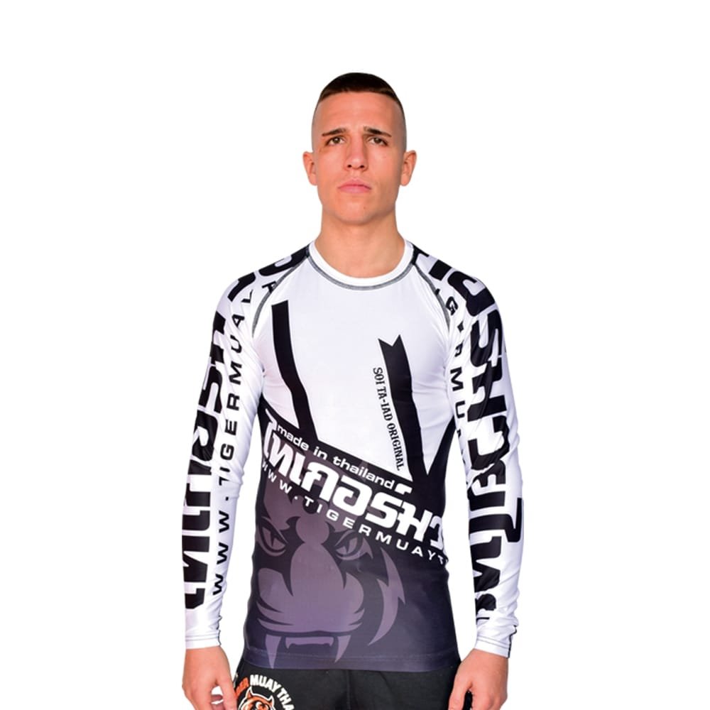 Camiseta deportiva Rash Guard de la marca "Tiger Muay Thai" de color blanco, gris y negro. Llevada por modelo con brazos estirados. Transpirable con diseño sublimado. Imagen frontal.