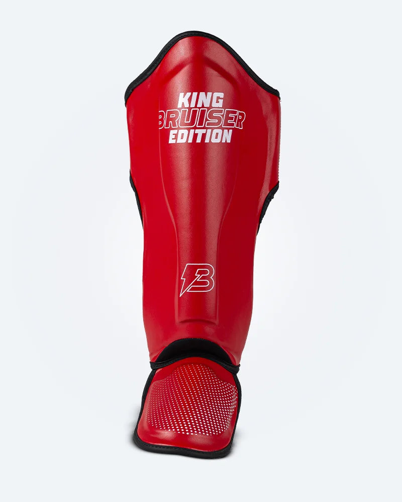 Espinillera de Muay Thai "King Bruiser Edition" color rojo con detalles blancos. Logo Bruiser en la parte frontal inferior, hecha de piel sintética, protección para espinillas, tobillos y pies para Kickboxing, MMA y entrenamiento de contacto. Imagen frontal.
