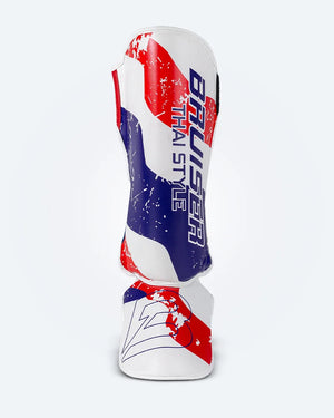 Espinillera de Muay Thai Bruiser blanca con diseño en azul y rojo inspirado en la bandera de Tailandia, logo Bruiser en la parte lateral, hecha de piel sintética, protección para espinilla y empeine para entrenamiento y kickboxing. Imagen frontal.