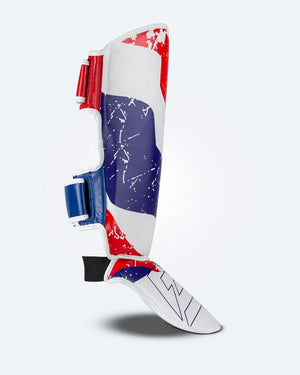 Perfil derecho de espinillera de kickboxing y muay thai, blanca con diseño en azul y rojo inspirado en la bandera de Tailandia, logo Bruiser en la parte frontal lateral y protección para espinilla y empeine para entrenamiento y kickboxing. Ajuste de velcro seguro.