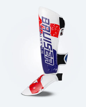Perfil izquierdo de espinillera de kickboxing y muay thai, blanca con diseño en azul y rojo inspirado en la bandera de Tailandia, logo Bruiser en la parte frontal lateral y protección para espinilla y empeine para entrenamiento y kickboxing. Ajuste de velcro seguro.