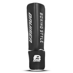 Espinillera de boxeo y muay thai negras con detalles blancos y logo Bruiser en la parte frontal lateral, hecha de polipiel con relleno de alta densidad que absorbe golpes y protege espinillas. Sistema de velcro reforzado para entrenamiento de contacto. Imagen frontal.