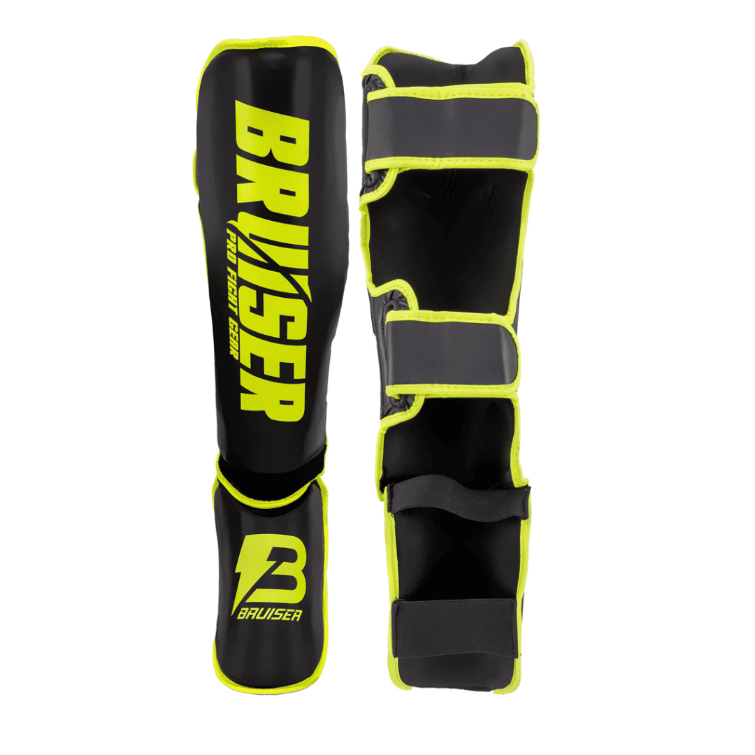 Espinilleras marca Bruiser por delante y por detrás color negro y amarillo. Logo en el centro. Hechas de polipiel con espuma absorbente. Imagen frontal.