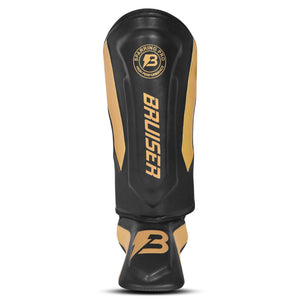 Espinillera marca Bruiser color negro y dorado. Logo en el centro. Hecha de microfibra y rellenas de espuma y latex. Cierres anchos de velcro.