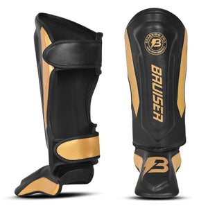 Espinilleras marca Bruiser por delante y por detrás color negro y dorado. Logo en el centro. Hechas de microfibra y rellenas de espuma y latex. Cierres anchos de velcro.