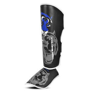 Espinilleras marca Tiger por delante color negro y azul. Logo en el centro. Hechas de polipiel con espuma absorbente. Perfil izquierdo.