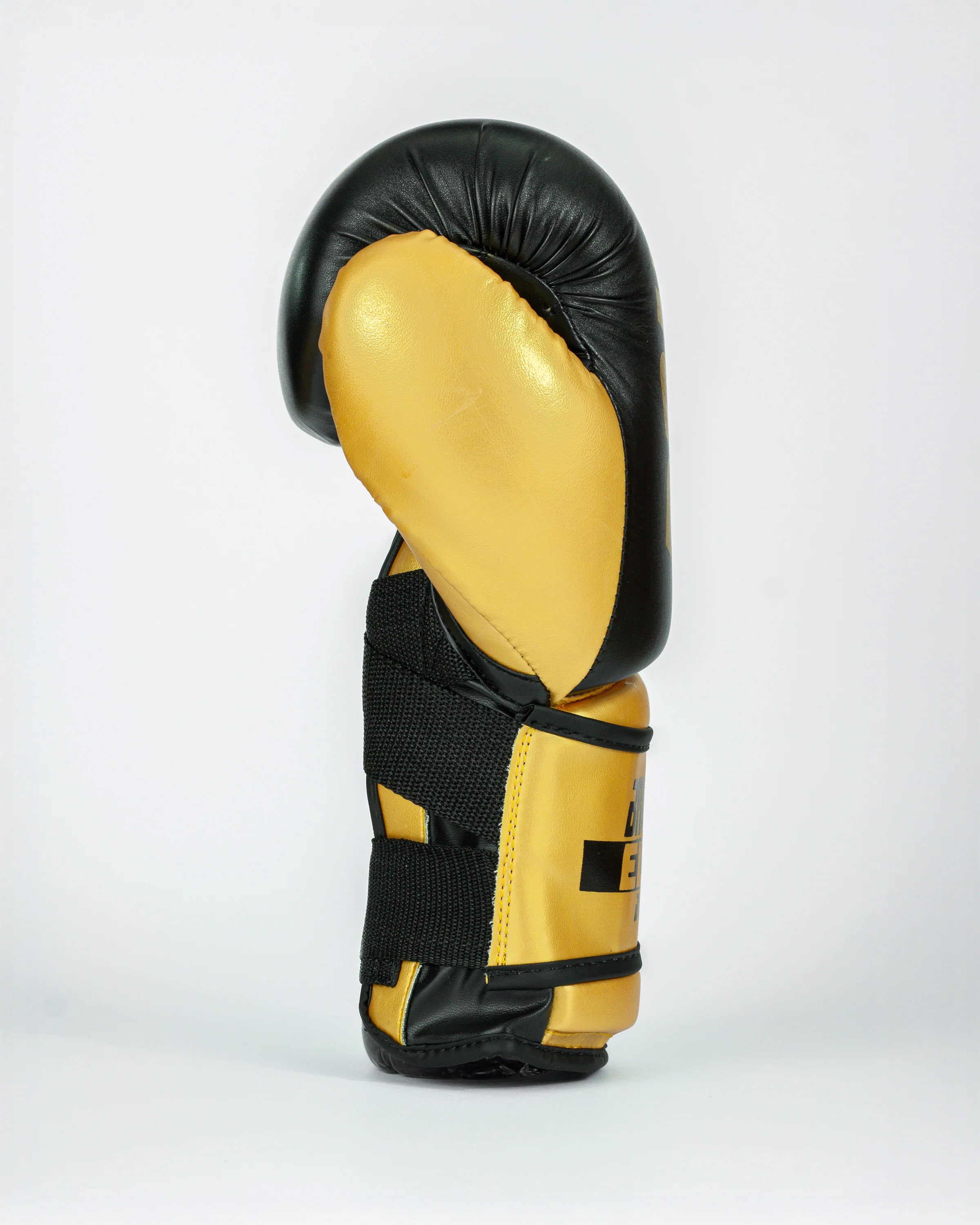 Guante de boxeo Bruiser color negro y dorado. Logo de la marca en el centro en vertical. Hecho de piel de vaca con acolchado interior denso. Cierre de velcro reforzado. Para kickboxing, muay thai. Perfil izquierdo.
