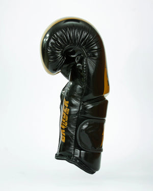 Guantes de boxeo Bruiser color negro y dorado. Logo de la marca en el centro en vertical. Hecho de polipiel resistente con acolchado interior. Cierre de velcro seguro. Para entrenamiento en saco y sparring controlado. Perfil izquierdo.