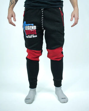 Pantalón de chándal negro con detalles rojos, estampado Bruiser en rojo blanco y azul, llevado por modelo de cintura con brazos estirados.