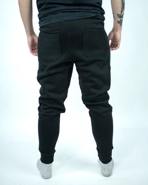 Parte trasera de pantalón de chándal negro, llevado por modelo de cintura con brazos estirados. Cintura elástica para mejor adaptación al cuerpo.