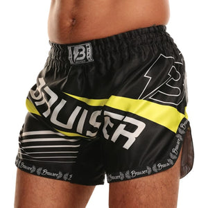 Pantalón deportivo Bruiser para Muay Thai color negro con detalles amarillos y logo "Bruiser" escrito en el centro de color blanco, llevado por modelo de cintura. Logo lateral sublimado. 100% poliéster, experiencia ligera. Cinturón elástico con costuras reforzadas. Imagen perfil izquierdo.