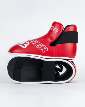Protectores de pie "Bruiser" color rojo para kickboxing, taekwondo o muay thai, uno encima del otro. Hechos de polipiel. Sistema de sujeción con elástico y cierre de velcro. Perfil izquierdo.