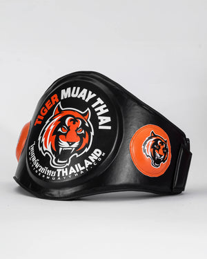 Ventral "TMT" color negro y naranja con logo en grande en la parte frontal. Hecho con materiales premium y relleno de alta densidad. Logo en los laterales. Ajuste cómodo y natural, velcro reforzado. Imagen lateral.