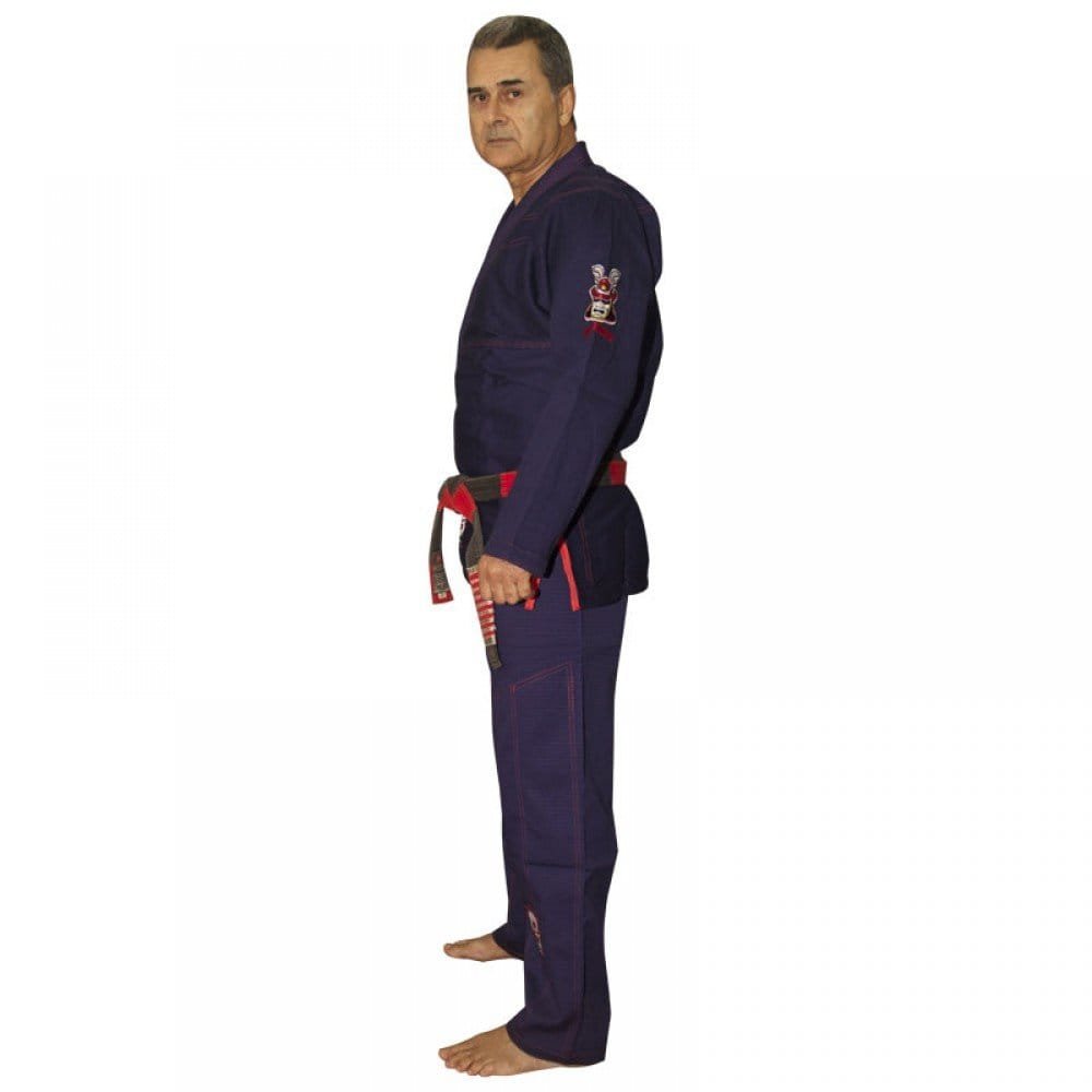 Kimono de Jiu Jitsu color azul marino con detalles rojos, llevado por modelo con brazos estirados mirando al frente con cinturón rojo y negro. Diseño bordado en la manga izquierda. Hecho de 100% algodón, ajuste perfecto. Imagen lateral. 