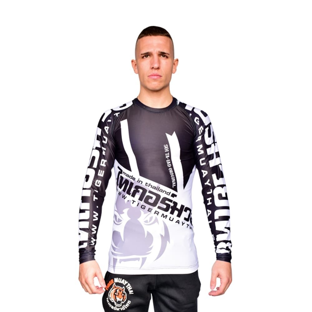 Camiseta deportiva Rash Guard de la marca "Tiger Muay Thai" de color blanco, gris y negro. Llevada por modelo con brazos estirados. Transpirable con diseño sublimado. Imagen frontal