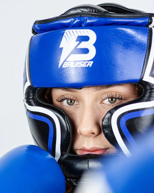 Casco Profesional Bruiser color azul y negro con rayas a los lados llevado por modelo. Logo en el centro. Diseñado con espuma densa y sistema de velcro ajustable. Diseño superior abierto. Imagen frontal de cerca.