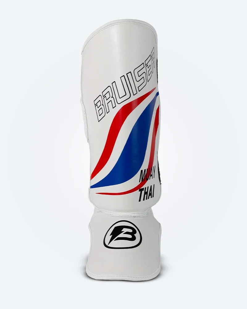 Espinillera de muay thai Bruiser blancas con diseño en azul y rojo inspirado en la bandera de Tailandia, logo Bruiser en la parte frontal y protección para espinilla y empeine para entrenamiento y kickboxing. Imagen frontal.