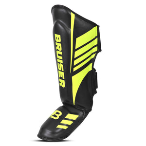 Parte lateral de espinilleras de kickboxing y muay thai, negras con detalles verde neón, diseño anatómico con protección para espinilla y empeine y cierre ajustable para entrenamiento y sparring.