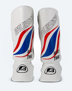 Espinilleras de muay thai Bruiser blancas con diseño en azul y rojo inspirado en la bandera de Tailandia, logo Bruiser en la parte frontal y protección para espinilla y empeine para entrenamiento y kickboxing. Imagen frontal.