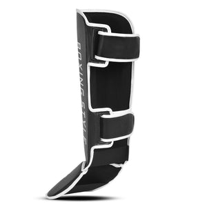Espinillera de boxeo y muay thai  negra con detalles blancos y logo Bruiser en la parte frontal lateral, hecha de polipiel con relleno de alta densidad que absorbe golpes y protege espinillas. Sistema de velcro reforzado para entrenamiento de contacto. Parte trasera.