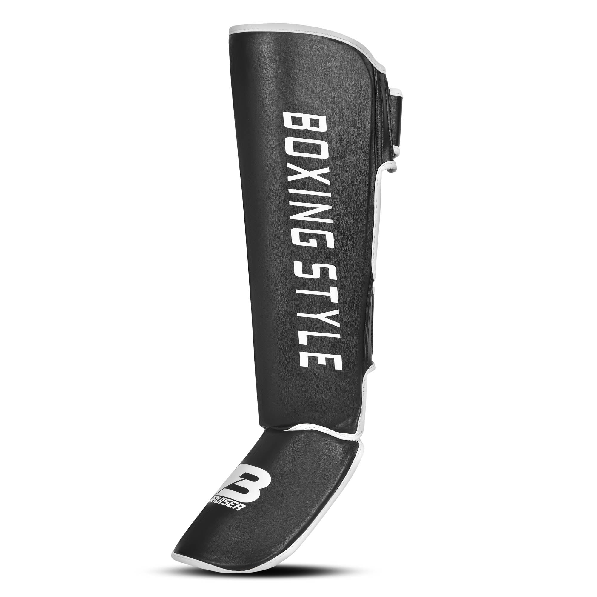 Espinillera de boxeo y muay thai  negras con detalles blancos y logo Bruiser en la parte frontal lateral, hecha de polipiel con relleno de alta densidad que absorbe golpes y protege espinillas. Sistema de velcro reforzado para entrenamiento de contacto. Perfil izquierdo.