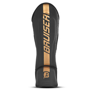 Espinillera marca Bruiser por delante y por detrás color negro y dorado. Logo en el centro. Hechas de piel sintética y rellena de espuma y látex. Doble cierre de velcro. 