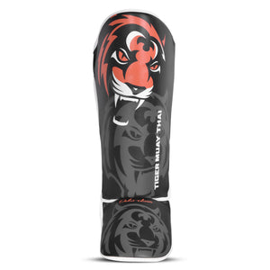 Espinillera marca Tiger para niños por delante color negro y naranja. Logo en el centro. Hecha de polipiel con espuma absorbente. 