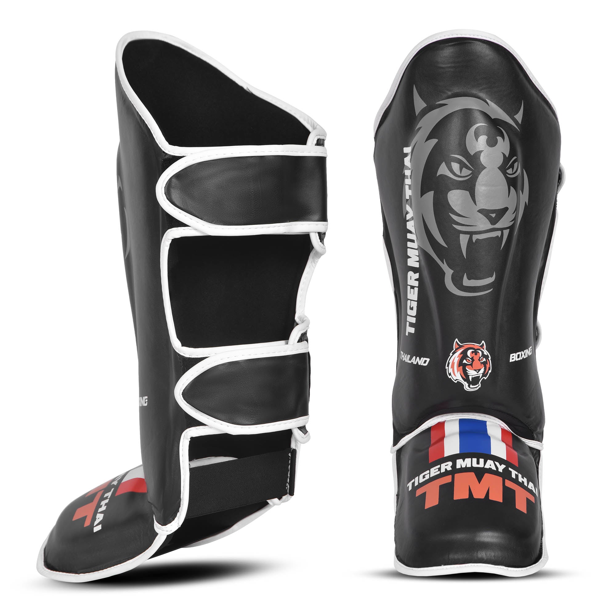 Espinilleras Tiger Muay Thai color negro con detalle naranjas. Logo de la marca en el centro. Hecha de polipiel con refuerzo en tibias y pies y espuma absorbente. Imagen frontal. 