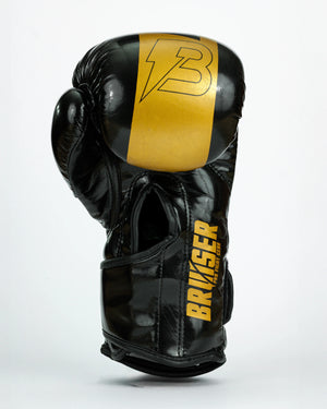Guantes de boxeo Bruiser color negro y dorado. Logo de la marca en puño. Hecho de polipiel resistente con acolchado interior. Cierre de velcro seguro. Para entrenamiento en saco y sparring controlado. Imagen frontal.