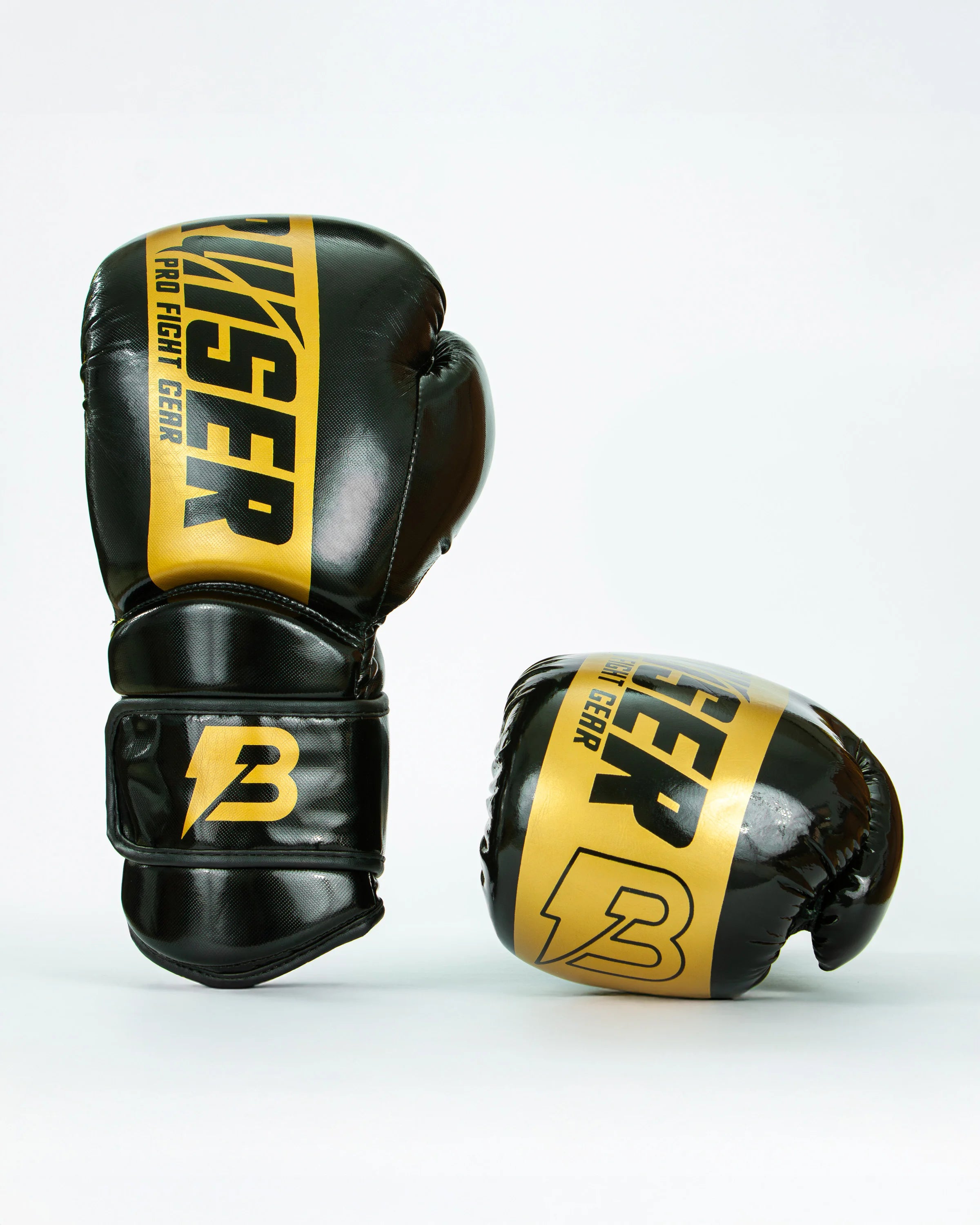 Guantes de boxeo Bruiser color negro y dorado, uno de pie y otro estirado. Logo de la marca en el centro en vertical. Hecho de polipiel resistente con acolchado interior. Cierre de velcro seguro. Para entrenamiento en saco y sparring controlado. 