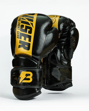 Guantes de boxeo Bruiser color negro y dorado. Logo de la marca en el centro en vertical. Hecho de polipiel resistente con acolchado interior. Cierre de velcro seguro. Para entrenamiento en saco y sparring controlado. 