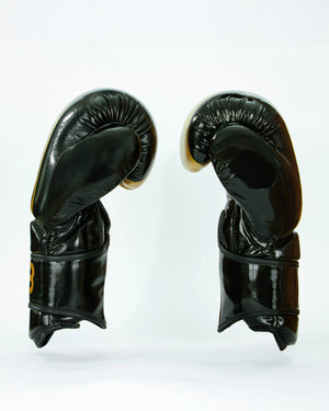 Guantes de boxeo Bruiser color negro y dorado. Logo de la marca en el centro en vertical. Hecho de polipiel resistente con acolchado interior. Cierre de velcro seguro. Para entrenamiento en saco y sparring controlado. 