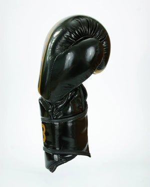 Guantes de boxeo Bruiser color negro y dorado. Logo de la marca en el centro en vertical. Hecho de polipiel resistente con acolchado interior. Cierre de velcro seguro. Para entrenamiento en saco y sparring controlado. Perfil derecho. 