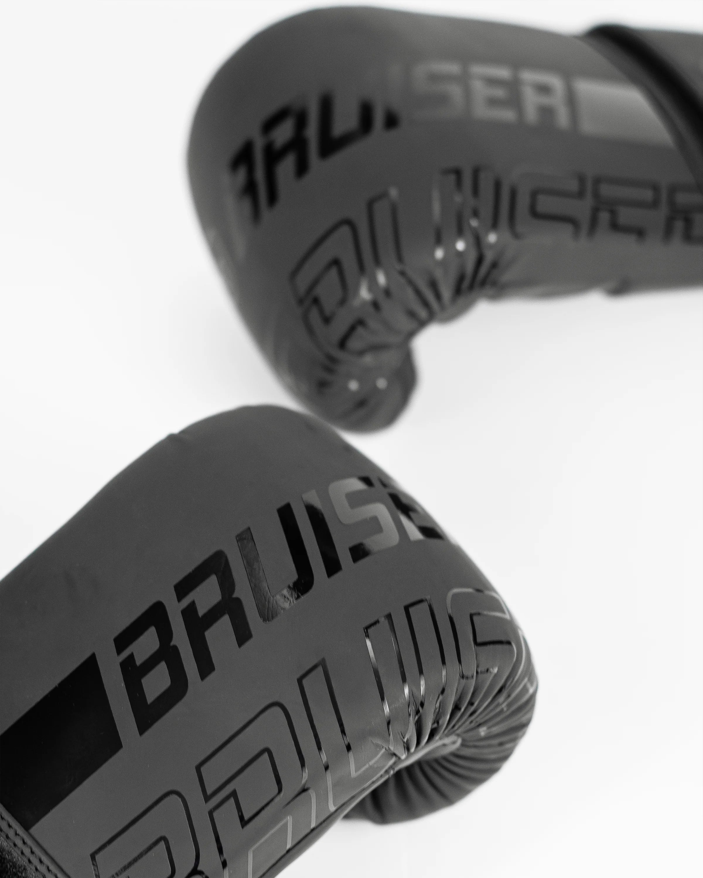 Par de guantillas Bruiser negras, logo brillante "Bruiser" en el centro en vertical. Hechas de polipiel resistente para entrenamientos frecuentes, golpeo en saco y manoplas. Imagen frontal.