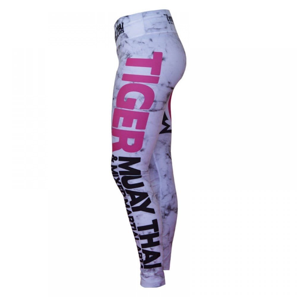 Mallas "TMT" color blanco con detalles negros y rosas. Logo en grande de color rosa en pierna izquierda. Hechas de poliester y spandex. Cordón de ajuste de cintura. Perfi izquierdo.