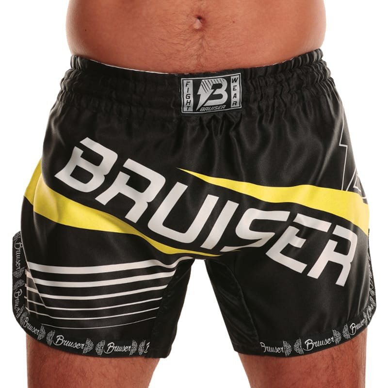 Pantalón deportivo Bruiser para Muay Thai color negro con detalles amarillos y logo "Bruiser" escrito en el centro de color blanco, llevado por modelo de cintura. 100% poliéster, experiencia ligera. Cinturón elástico con costuras reforzadas. Imagen frontal.