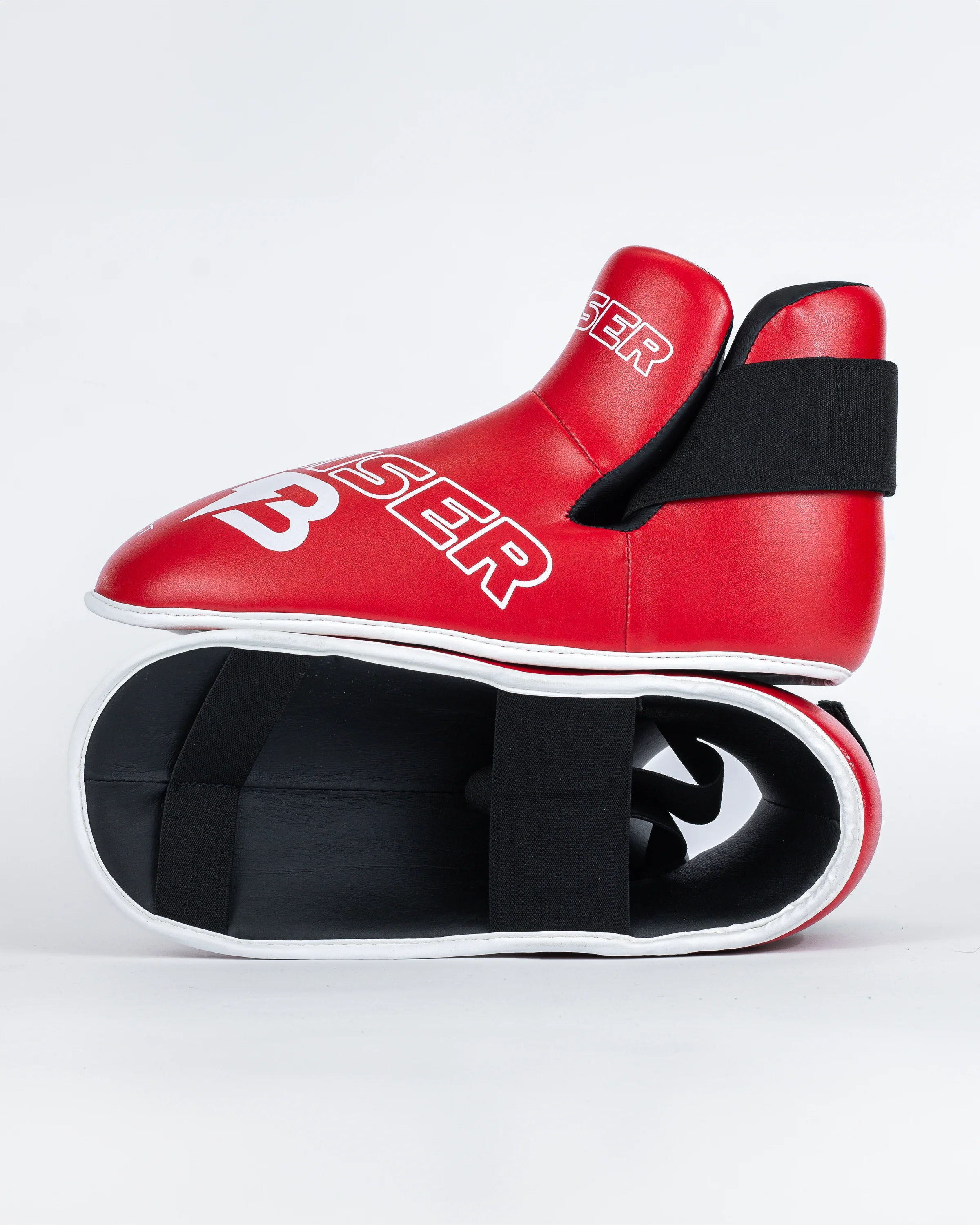 Protectores de pie "Bruiser" color rojo para kickboxing, taekwondo o muay thai, uno encima del otro. Hechos de polipiel. Sistema de sujeción con elástico y cierre de velcro. Perfil izquierdo.
