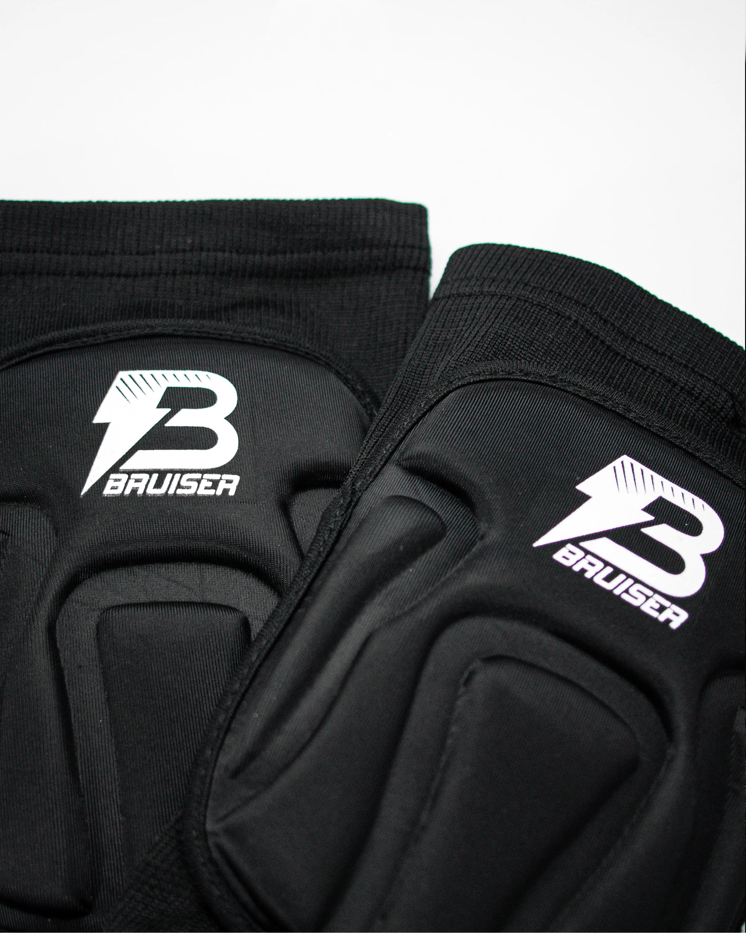 Par de rodilleras Bruiser de color negro. Una detrás de otra. Logo en el centro. Protección, comodidad y libertad de movimiento seguras. Para sparring, BJJ y MMA. Imagen frontal.