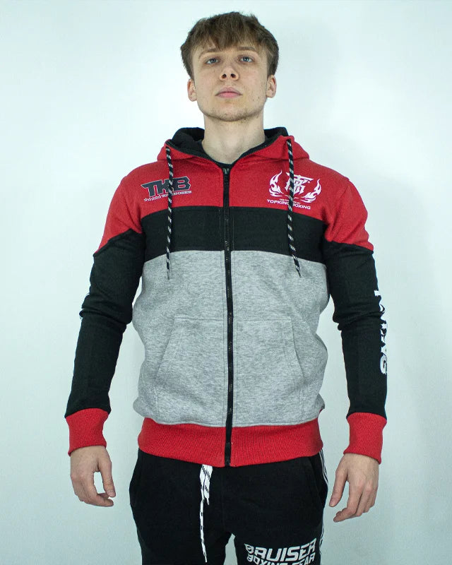 Sudadera con cremallera Top King roja, negra y gris, llevada por modelo con brazos estirados mirando al frente. Logo en negro en parte superior izquierda y blanco en parte superior derecha. 
