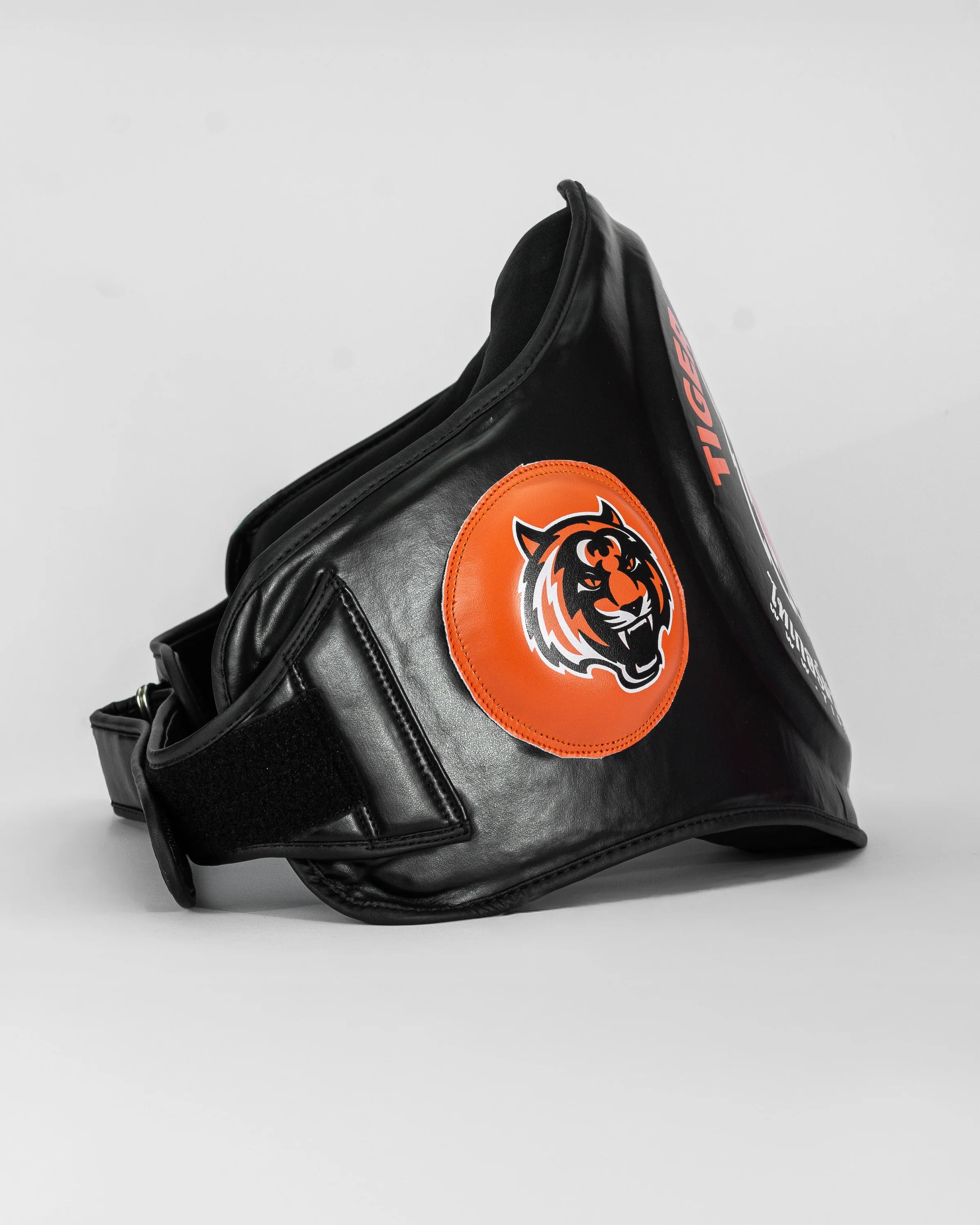 Ventral "TMT" color negro y naranja. Hecho con materiales premium y relleno de alta densidad. Logo en los laterales. Ajuste cómodo y natural, velcro reforzado. Imagen lateral.  